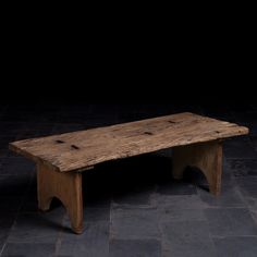 an old wooden bench sitting on top of a stone floor in front of a black wall