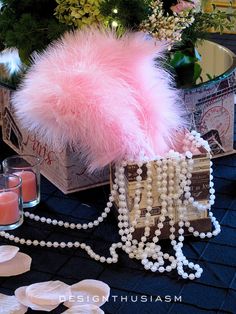 a table topped with pearls and candles next to a pink fur ball on top of a box