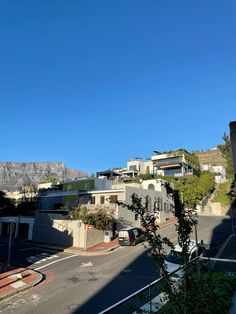 an empty street with houses on the hill in the back ground and mountains in the background