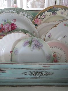 a bunch of plates that are sitting in a box on the counter top with flowers painted on them