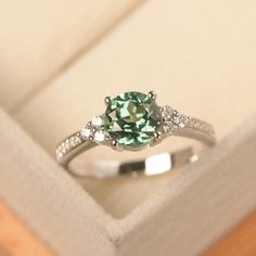 an engagement ring with a green stone surrounded by white diamonds in a box on top of a wooden table