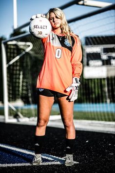 a woman in an orange jersey is holding a soccer ball and posing for the camera