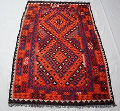 an orange and blue area rug on a white surface with fringes around the edges