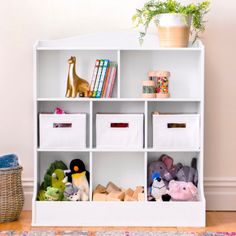 a white bookcase filled with lots of stuffed animals and toy storage bins next to a potted plant