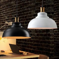 two black and white lamps hanging over a table with a laptop on it, in front of a brick wall