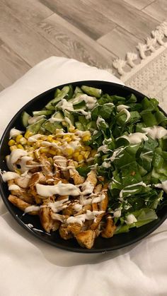 a black plate filled with salad and dressing on top of a white cloth next to a wooden table