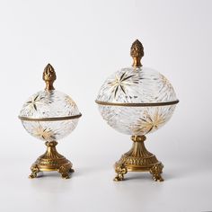 two glass covered dishes sitting next to each other on top of a white tablecloth