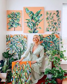 a woman is sitting on a bench in front of some plants and paintings that are hanging on the wall