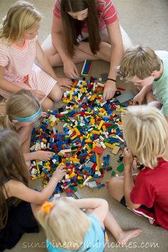 a woman sitting on the floor surrounded by children playing with legos