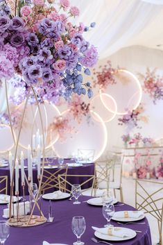 a table with purple and white flowers on it is set for a formal dinner or party