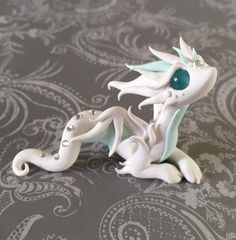 a white dragon figurine sitting on top of a gray tablecloth with paisley designs