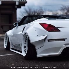 the back end of a white sports car parked in a parking lot next to a building