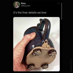 a hand holding a blue ceramic teapot with paw prints on it's side