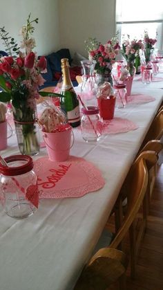 the table is set with pink and red flowers in vases, wine bottles, and napkins