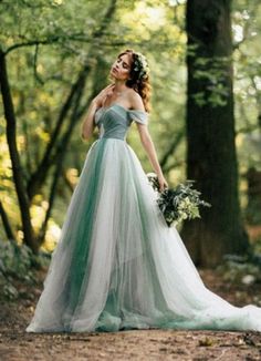 a woman in a green and white dress standing in the woods with her hands on her hips