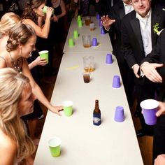 a group of people standing around a long table with cups on it and one man in a tuxedo