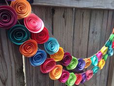 colorful rolled paper flowers are hanging on a wooden fence with wood slats in the background