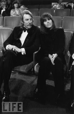 black and white photograph of two people sitting in an auditorium with their hands on their hipss