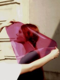 a woman is holding up a pink piece of paper with her face in the background