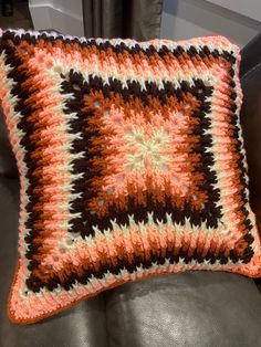 a crocheted pillow sitting on top of a leather couch next to a window