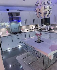 a modern kitchen with white cabinets and stainless steel appliances, including an island table surrounded by clear acrylic chairs