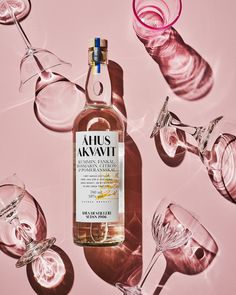 a bottle of alcohol sitting next to wine glasses on a pink background with the words ahus kavai written in gold