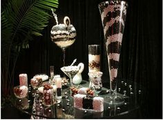 a table topped with lots of cakes and desserts next to tall glasses filled with liquid