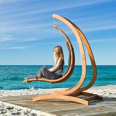 a woman is sitting on a wooden chair at the beach