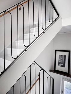 a white staircase with black handrails in a room next to a window and framed photograph on the wall