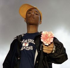 a man in a yellow hat holding a pink flower and looking up at the sky