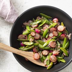 a black bowl filled with vegetables next to a wooden spoon on top of a white table