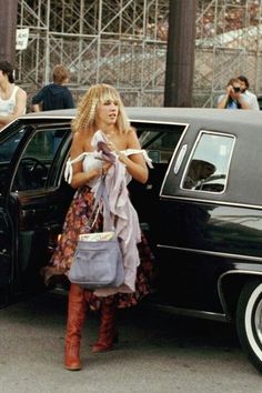 a woman standing next to a black car with her hand in the door and holding a purse