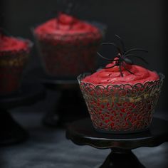 three red cupcakes sitting on top of a black cake stand with spider web decorations