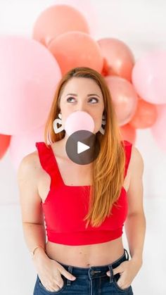 a woman wearing a red crop top and blue jeans is standing in front of balloons