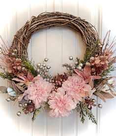 a wreath with pink flowers and greenery hanging on a door