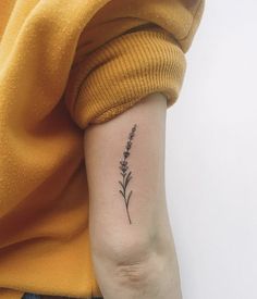 a woman's arm with a small lavender flower tattoo on the left inner arm