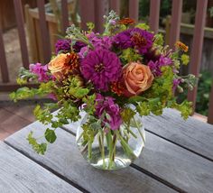 a glass vase filled with purple and orange flowers on top of a wooden table next to a fence