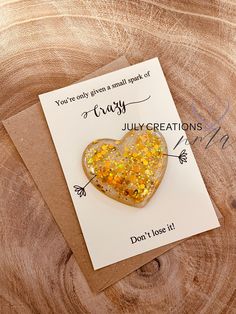 a card with a heart shaped brooch sitting on top of a piece of wood