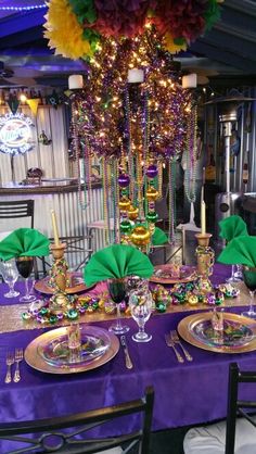 a purple table cloth with green napkins and gold place settings on it is set for a festive dinner