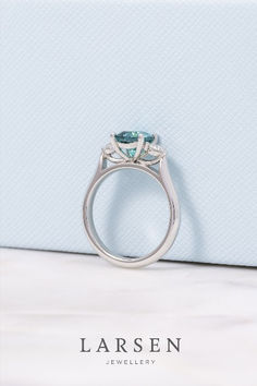 a blue diamond ring sitting on top of a white table next to a light blue box