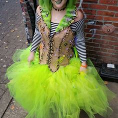 a woman dressed in green and black is standing next to a brick wall wearing a costume