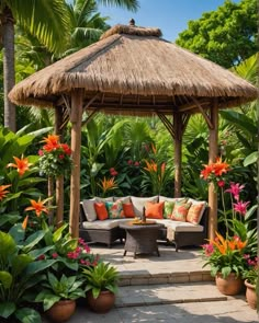 an outdoor seating area surrounded by tropical plants and flowers, with a thatched roof