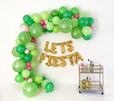 the balloon arch is decorated with green, pink and white balloons that spell out let's fiesta