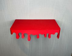 a red shelf with dripping paint on the top and bottom, against a white wall