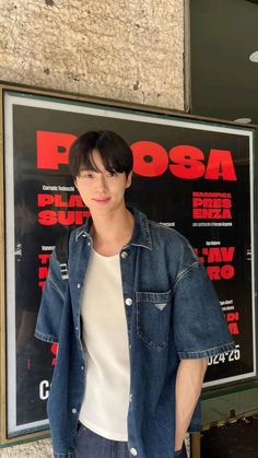 a man standing in front of a movie poster with his hands in his pockets and looking at the camera