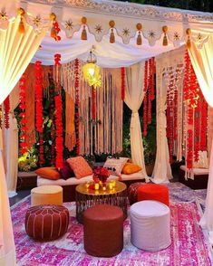 an outdoor seating area decorated with white drapes, red and orange decorations and pom poms hanging from the ceiling