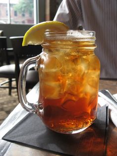 a mason jar filled with iced tea and lemon wedged into the top, sitting on a table