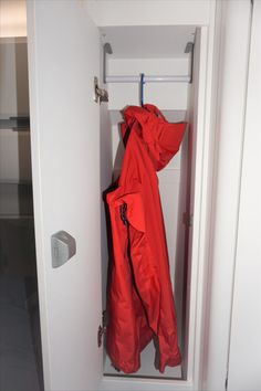 an open white closet with a red coat hanging from it