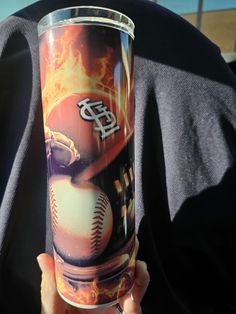 a person holding up a plastic cup with a baseball on it and flames in the background