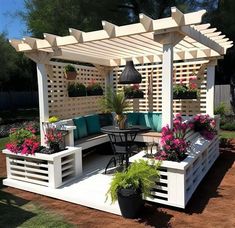 an outdoor seating area with potted plants and flowers on the table, in front of a pergolated wall